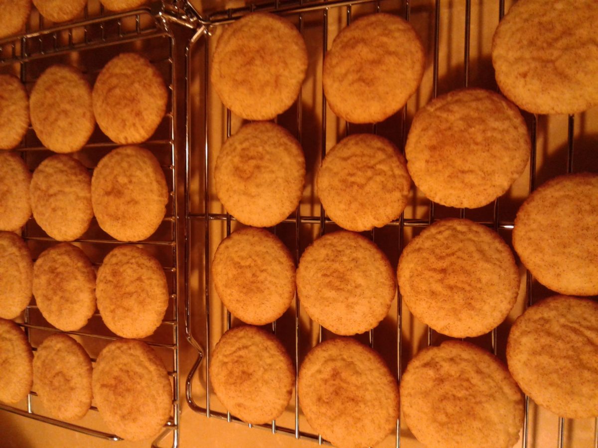 A batch of golden brown snickerdoodle cookies cooling on a wire rack.